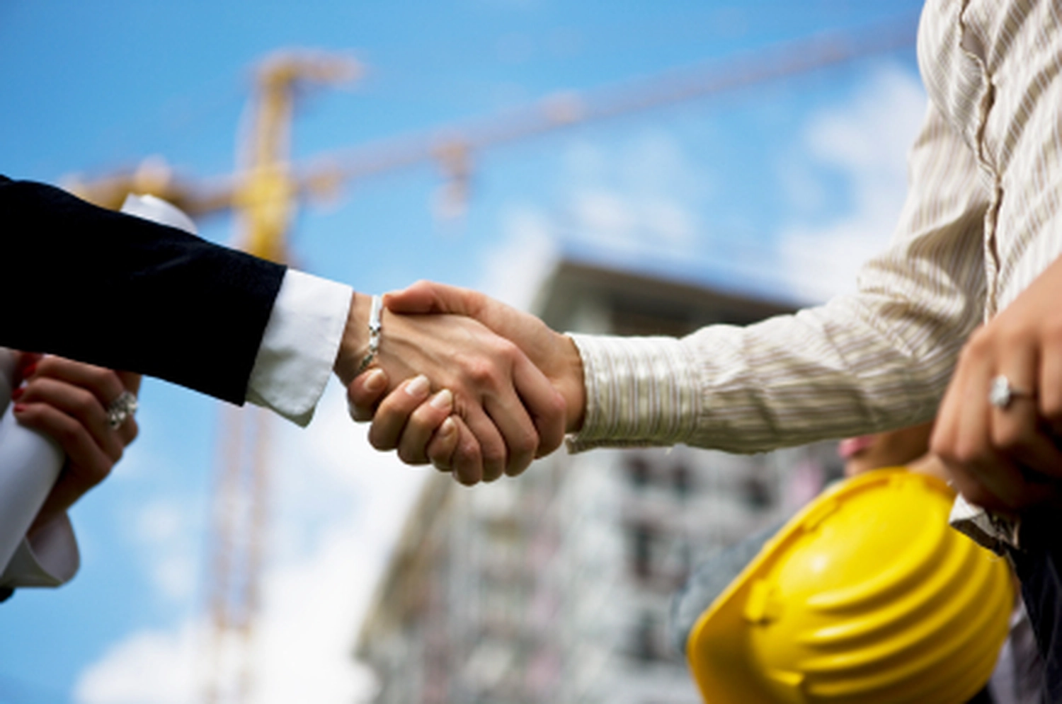 EB BAU SERVICE GmbH – Bauunternehmen – Zwei Personen schütteln sich vor einer Baustelle die Hände, um eine abgeschlossene Vereinbarung oder Partnerschaft zu symbolisieren.