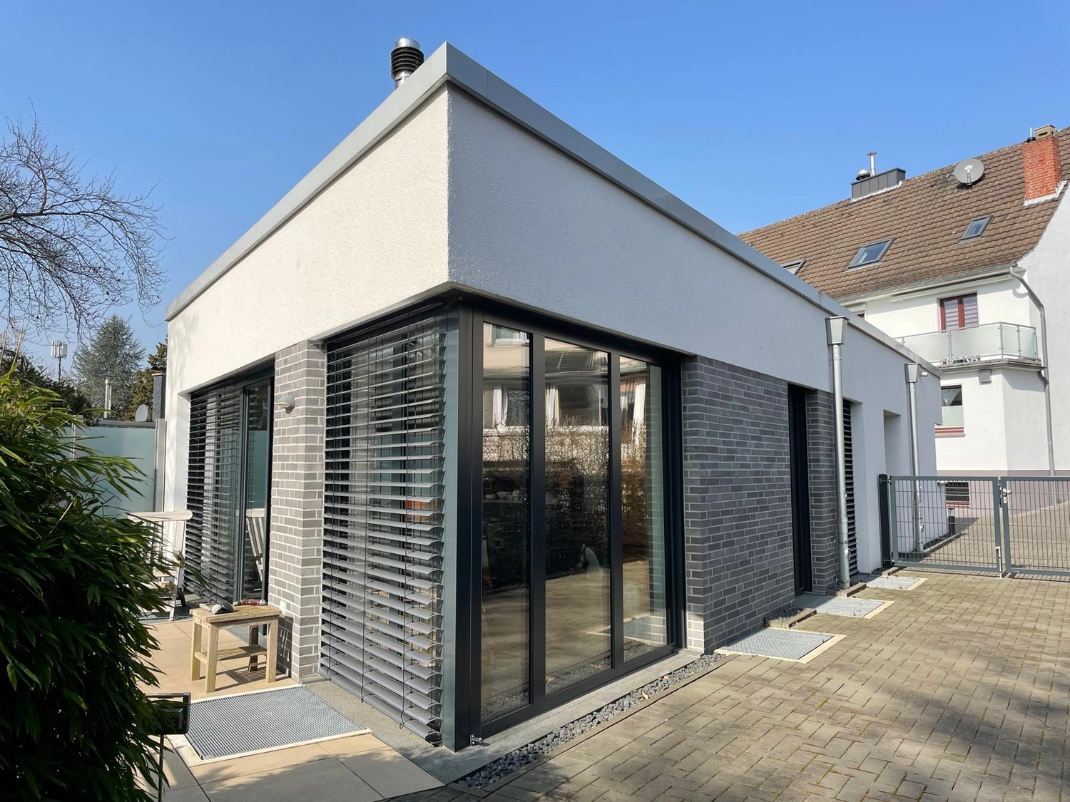EB BAU SERVICE GmbH – Bauunternehmen – Dieser moderne Wohnanbau zeichnet sich durch graues Backsteinmauerwerk und große Eckfenster mit verstellbaren Außenjalousien aus.